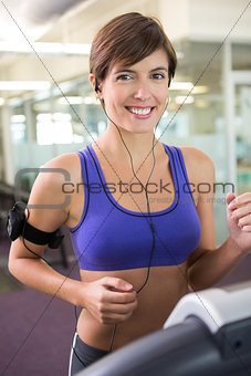 Fit brunette running on the treadmill listening to music