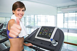 Fit brunette smiling at camera on the treadmill showing thumbs up