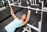 Fit brunette lifting heavy barbell lying on bench