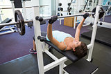 Fit brunette lifting heavy barbell lying on bench