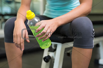 Fit woman sitting on bench holding energy drink