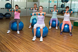 Fitness class holding dumbbells on exercise balls in studio
