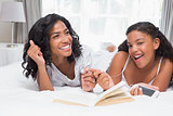 Mother and daughter reading book and listening to music together on bed