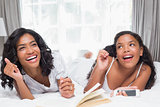 Mother and daughter reading book and listening to music together on bed