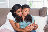Happy mother and daughter using smartphone together on sofa