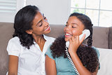 Happy mother and daughter on the phone together on sofa