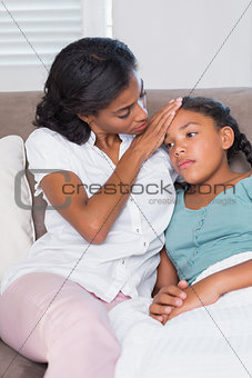 Concerned mother touching her daughters forehead