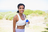 Fit woman holding sports bottle smiling at camera
