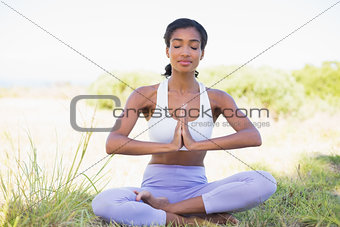 Fit woman sitting on grass in lotus pose with eyes closed