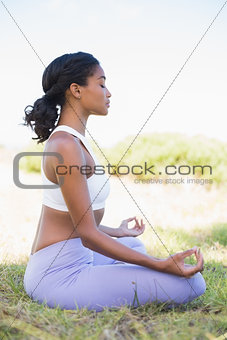 Fit woman sitting on grass in lotus pose with eyes closed