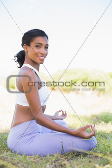 Fit woman sitting on grass in lotus pose smiling at camera