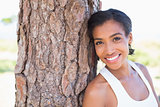 Fit woman leaning against tree smiling at camera