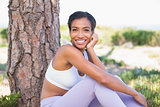 Fit woman sitting against tree smiling at camera