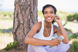 Fit woman sitting against tree listening to music