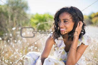 Happy pretty woman sitting on the grass in floral dress