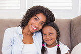 Pretty mother sitting on the couch with her daughter smiling at camera