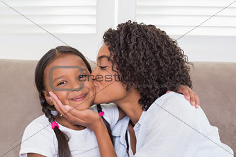 Pretty mother sitting on the couch with her daughter smiling at camera