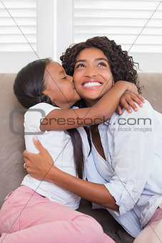 Pretty mother sitting on the couch with her daughter kissing her cheek