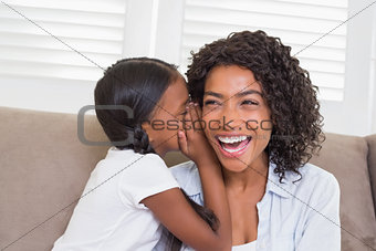 Pretty mother sitting on the couch with her daughter whispering a secret