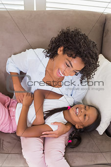 Pretty mother sitting on the couch tickling daughter