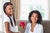 Pretty mother sitting on the couch with her daughter offering roses