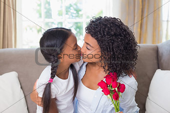 Pretty mother sitting on the couch kissing her daughter holding roses
