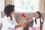 Pretty mother sitting on the couch with her daughter offering roses