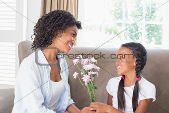 Pretty mother sitting on the couch with her daughter offering flowers