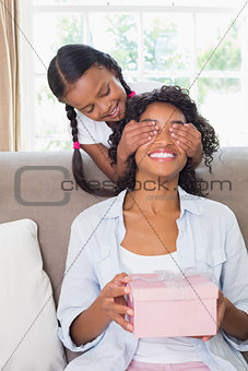 Pretty mother sitting holding gift with her daughter covering her eyes