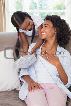 Pretty mother sitting on couch with daughter offering a gift