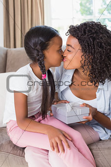 Pretty mother sitting on couch offering daughter a gift