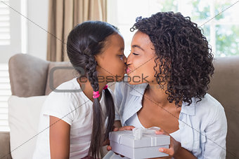 Pretty mother sitting on couch offering daughter a gift