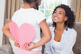 Pretty mother sitting on couch with daughter hiding heart card