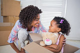 Cute daughter sitting in moving box holding teddy with mother