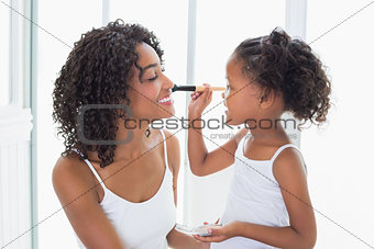 Cute daughter putting makeup on her mothers face