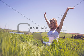 Pretty blonde sitting on grass using her laptop and cheering