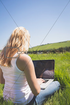 Pretty blonde sitting on grass using her laptop