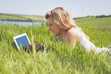 Pretty blonde lying on grass using her tablet