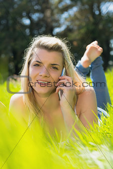Pretty blonde lying on grass talking on phone smiling at camera
