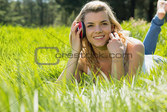 Pretty blonde lying on grass with headphones around neck