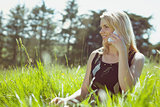 Pretty blonde in sundress sitting on grass talking on phone
