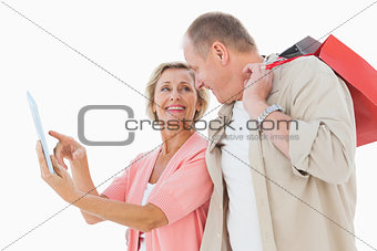 Smiling older couple holding shopping bags looking at tablet pc