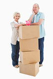 Older couple smiling at camera with moving boxes and piggy bank
