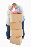 Older couple smiling at each other with moving boxes and piggy bank