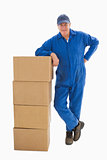 Happy delivery man leaning on pile of cardboard boxes