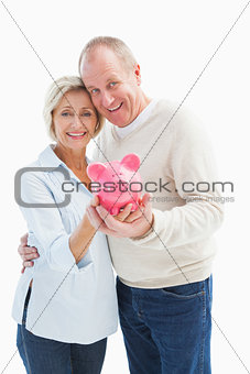 Happy mature couple smiling at camera showing piggy bank