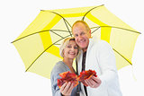 Happy mature couple showing autumn leaves under umbrella
