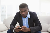 Handsome businessman sitting on couch sending text