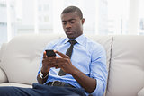 Handsome businessman sitting on couch sending text