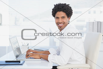 Handsome casual businessman smiling at camera working on laptop